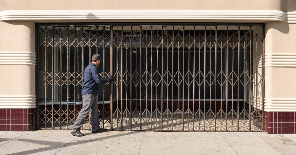 Shopkeeper drawing a scissor security gate across a period storefront