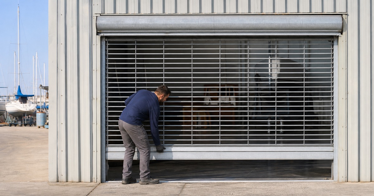 Technician setting the bottom bar of a roll-up steel door at a boatyard workshop