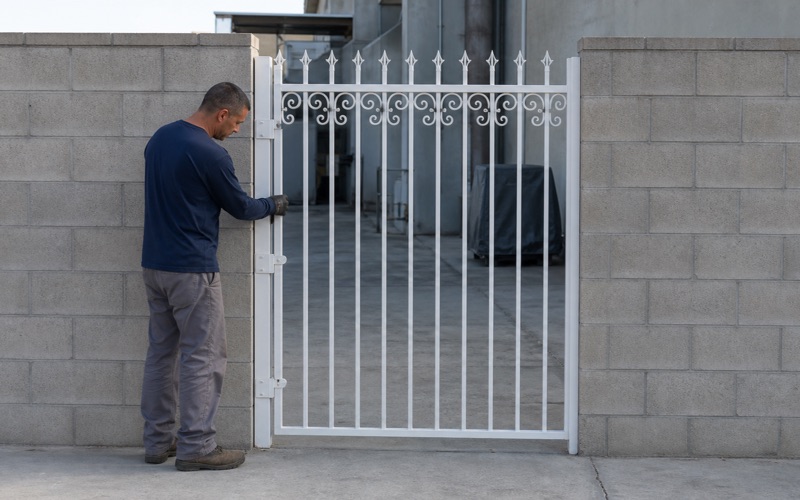 Fabricator checking picket spacing on a hung white ornamental iron gate